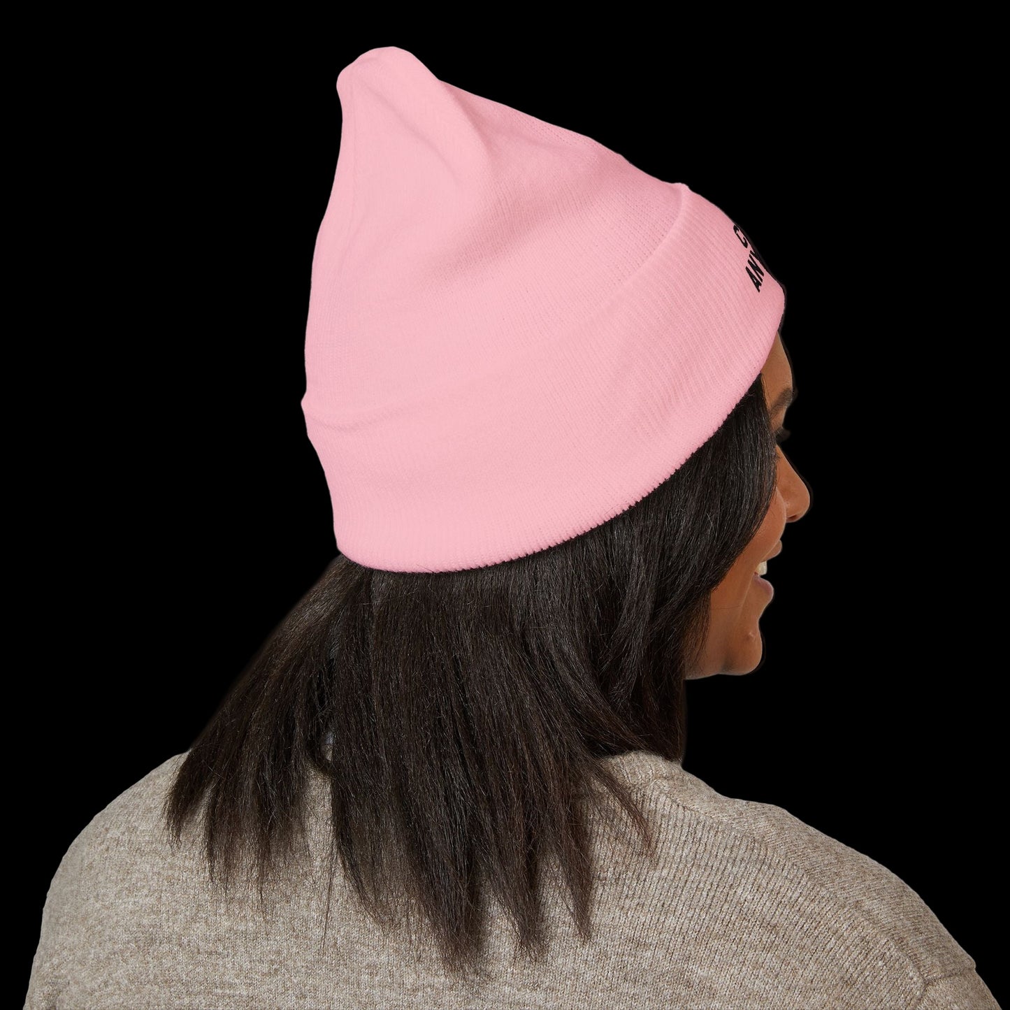 Person wearing a pink beanie with a brand logo on a black background