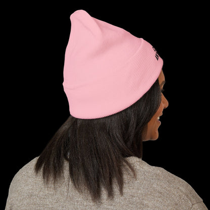Person wearing a pink beanie with a brand logo on a black background