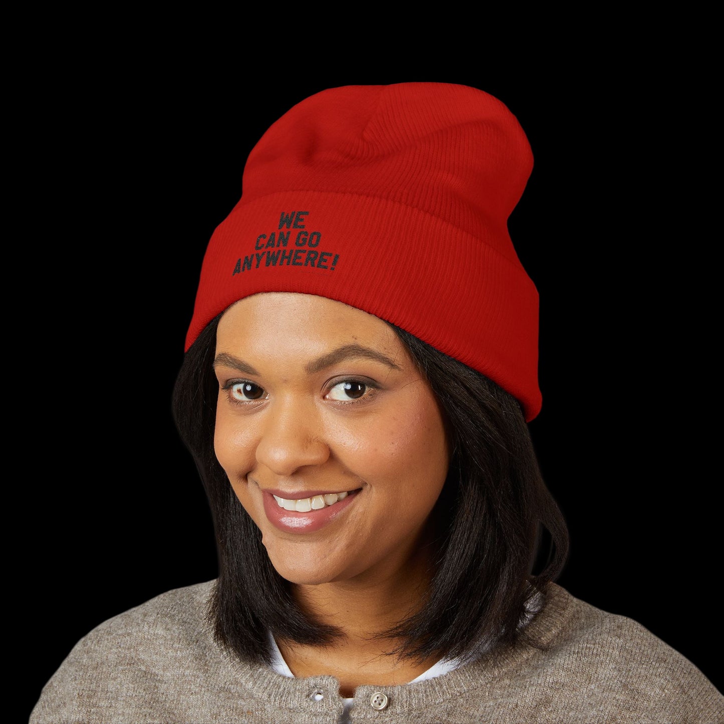 Person wearing a red beanie with text, smiling against a black background