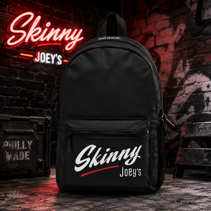 A black backpack with 'Skinny Joey's' branding in white and red, displayed in a gritty urban setting with a matching neon sign in the background.