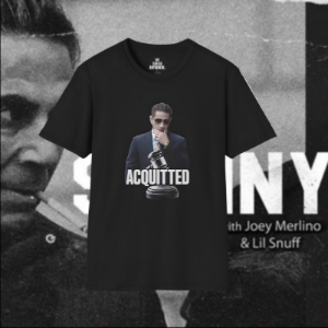 A black short-sleeve graphic t-shirt featuring a printed image of a man in a suit with a microphone and the word 'ACQUITTED' on the front, displayed against a black-and-white music poster background.