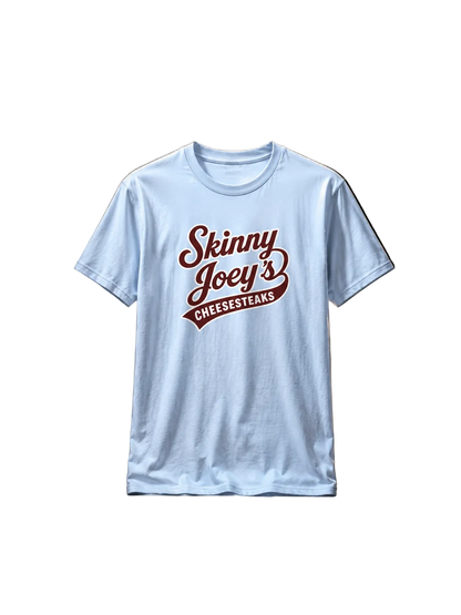 A light blue crewneck t-shirt featuring a dark red graphic print on the front that reads 'Skinny Joey's CHEESESTEAKS' in a stylized cursive and banner font, displayed against a plain white background.