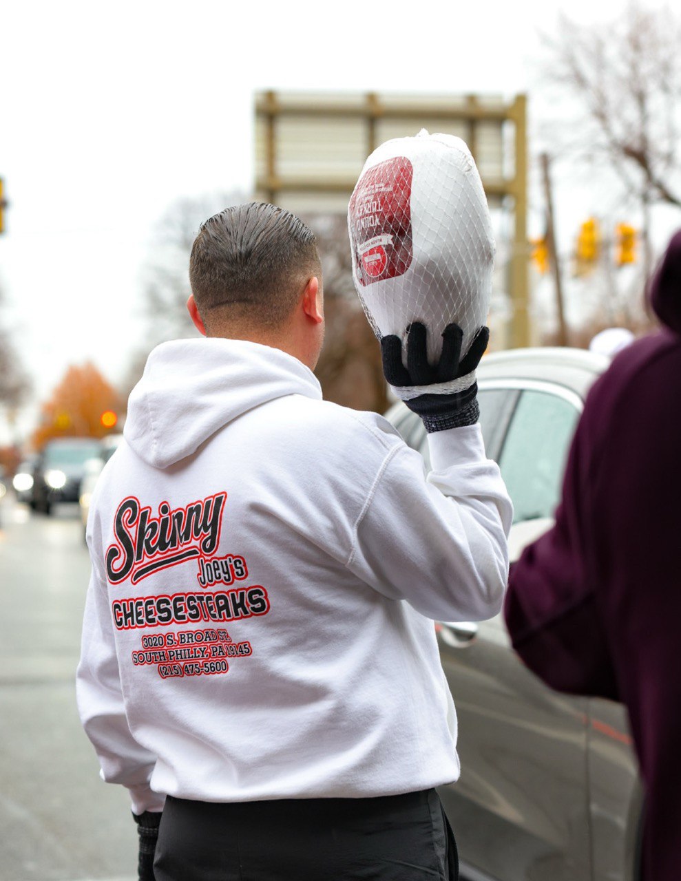 Person wearing a white hoodie with text, holding up a product in an urban setting.